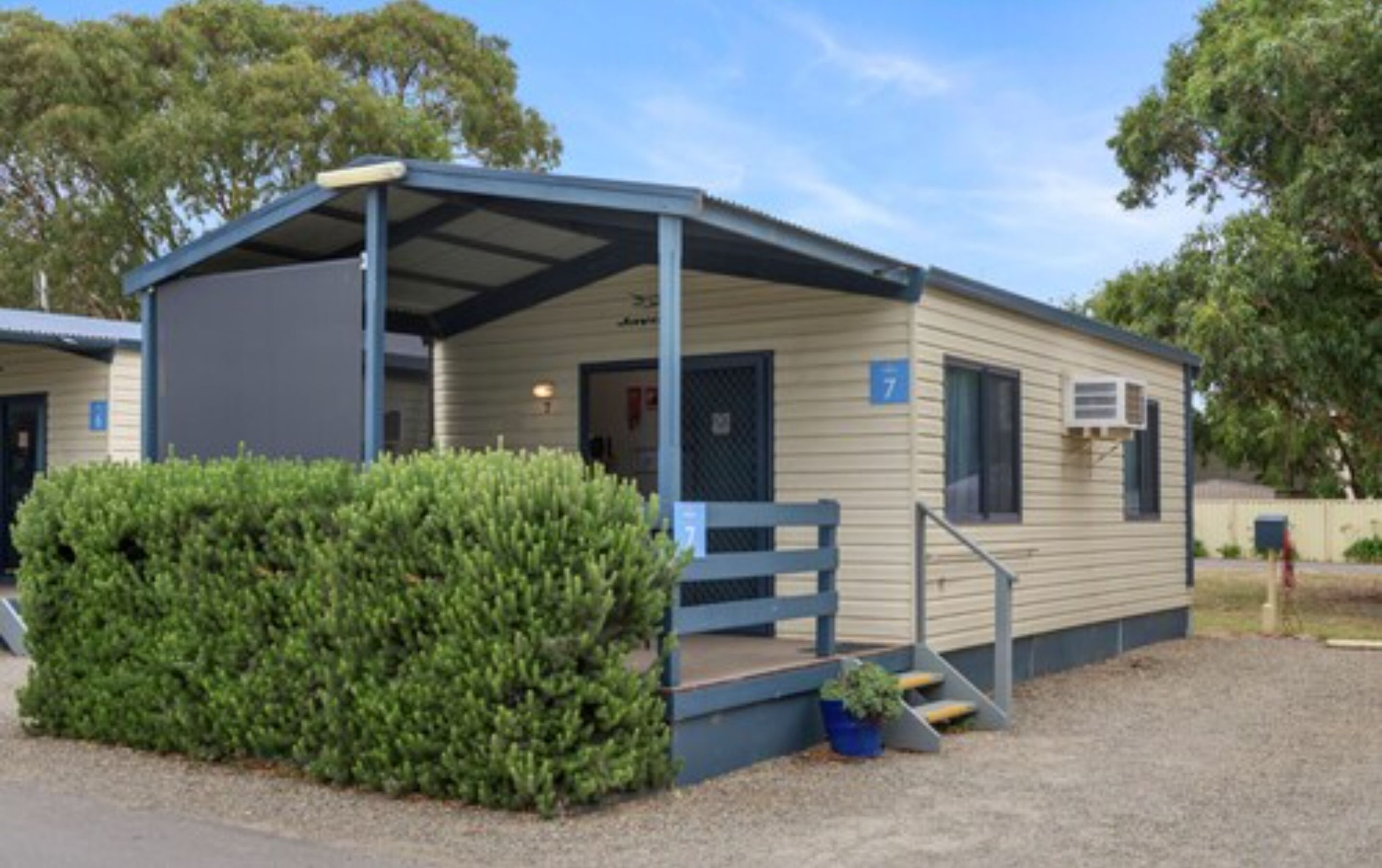 Une maison mobile de plain-pied, dotée d’un porche couvert, d’un petit jardin devant et d’une enseigne portant le chiffre 7.