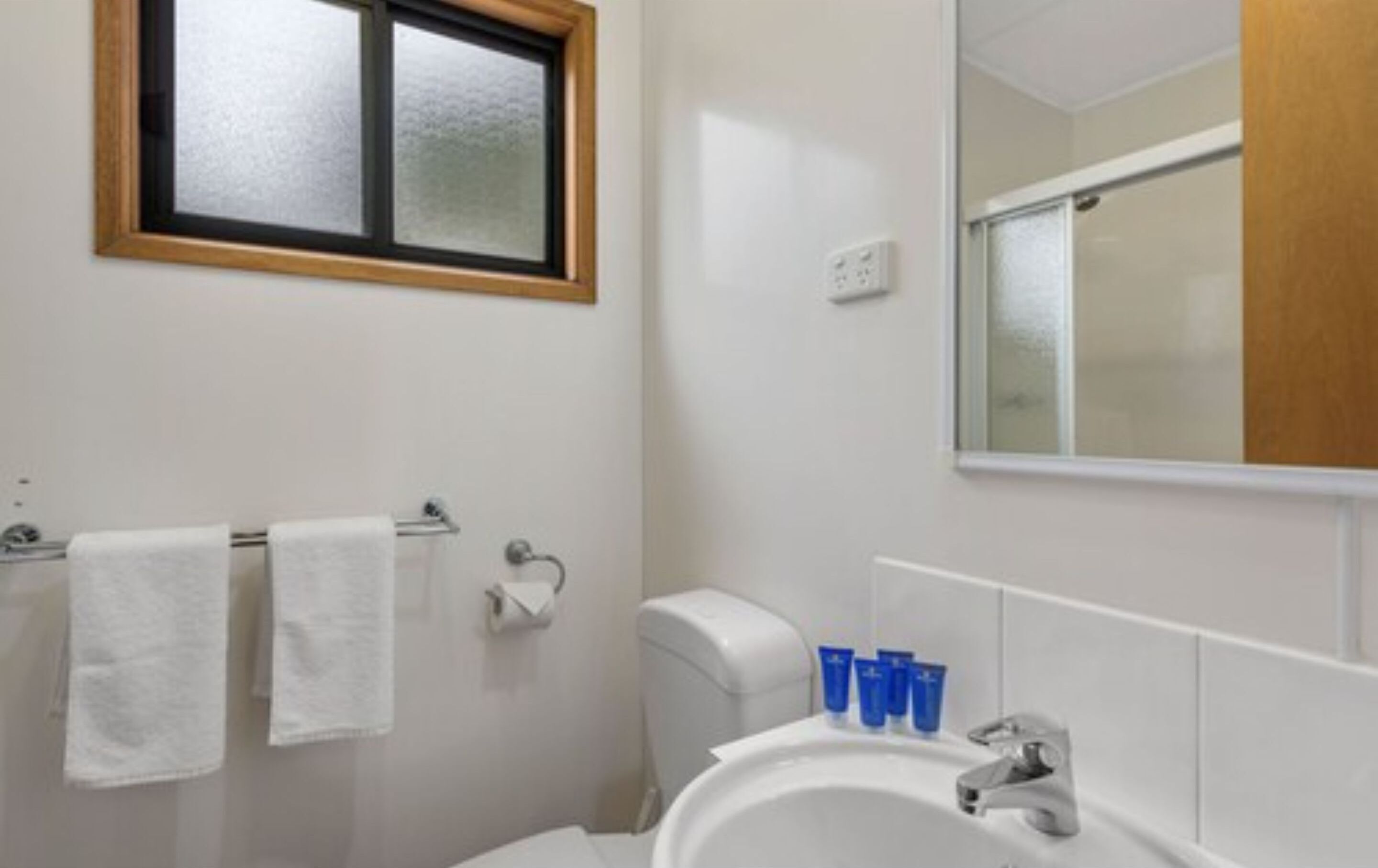 A bathroom with a toilet, sink, and a window above the mirror.