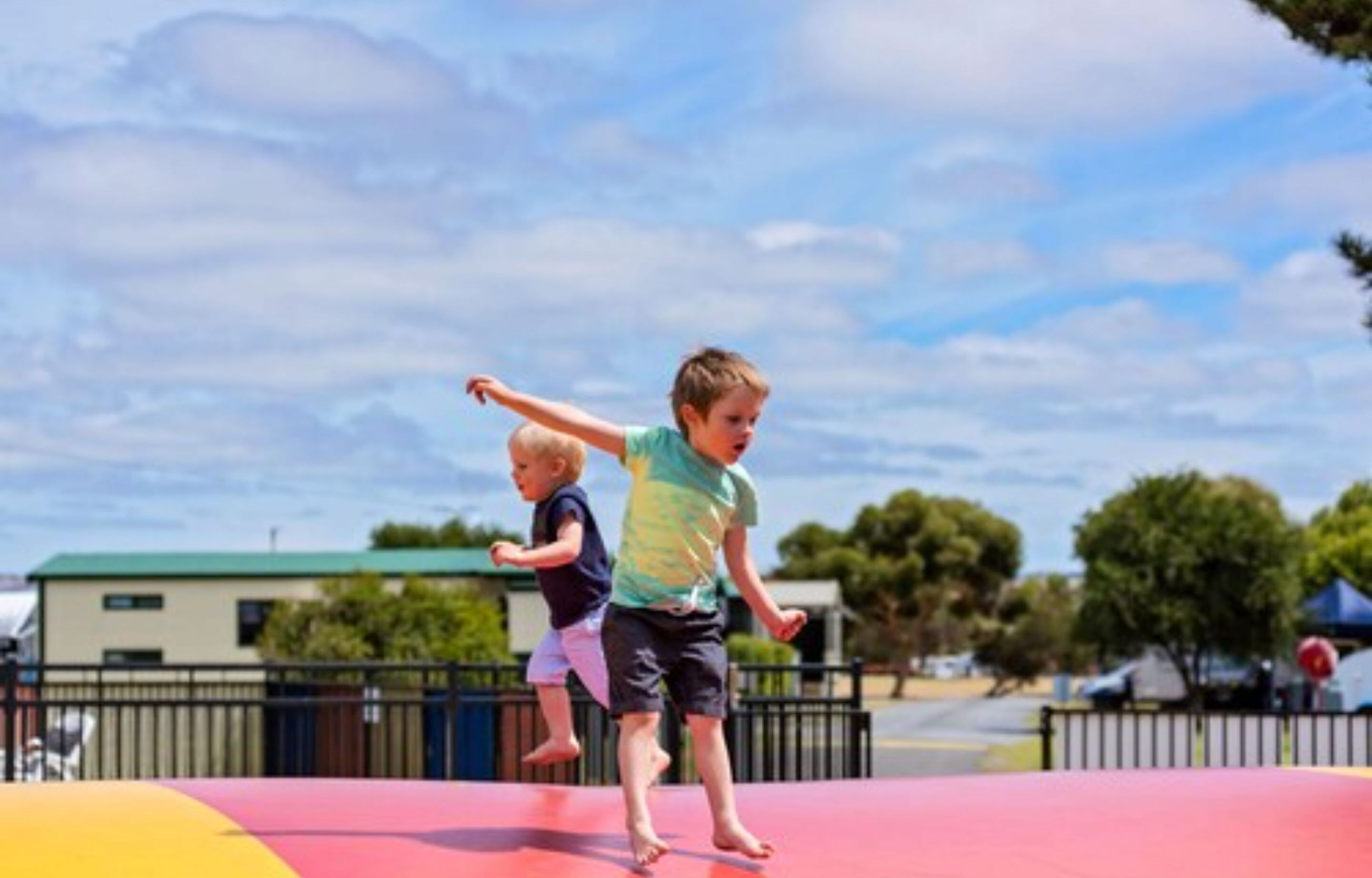 Two children playing on a colorful trampoline in an outdoor setting.
