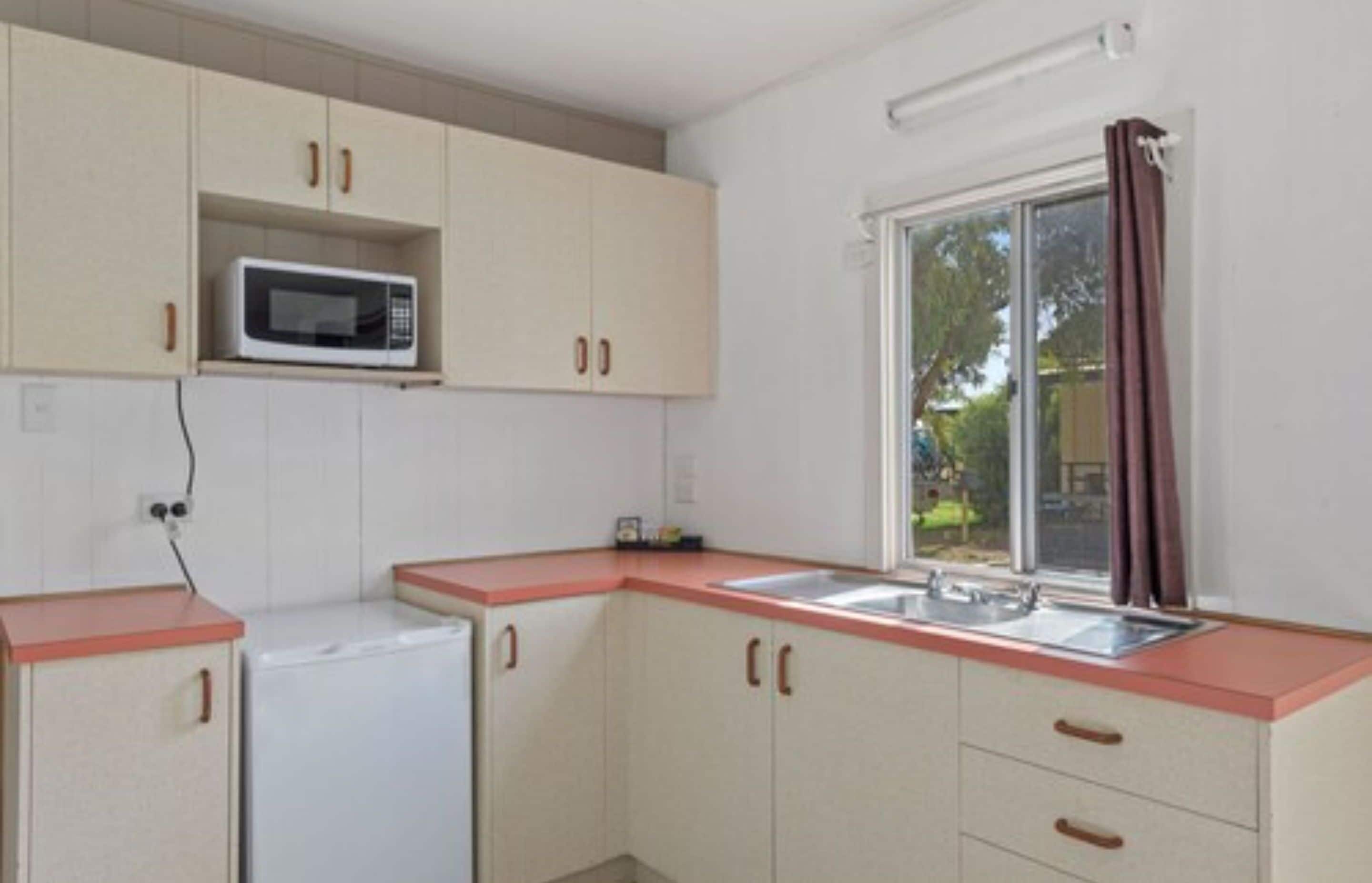Cocina pequeña equipada con microondas, refrigerador, lavamanos y armarios.