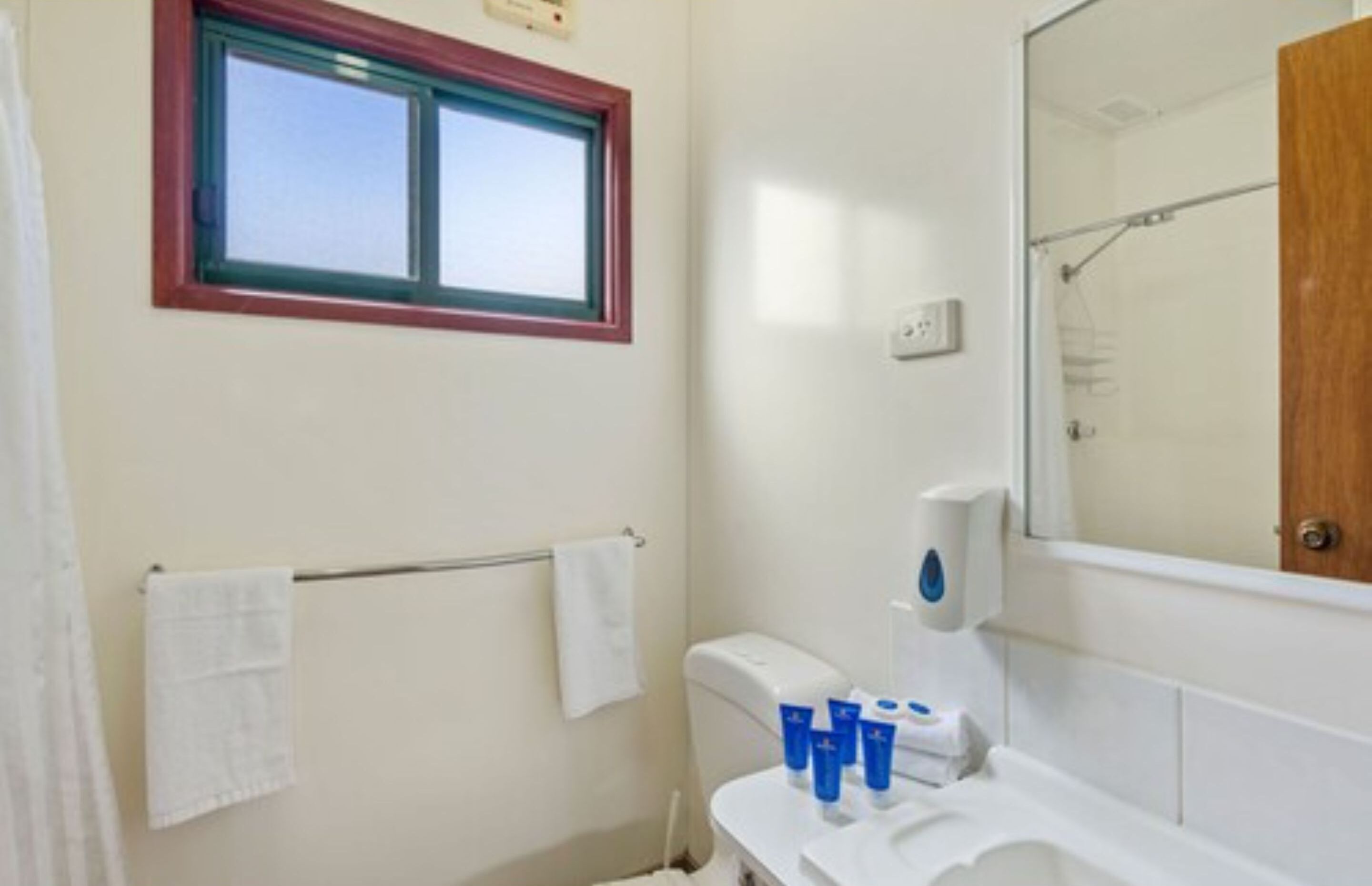 Een badkamer met een raam, een handdoekhouder, een toilet en een wastafel met toiletartikelen.