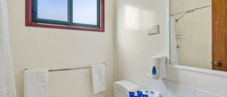 Een badkamer met een raam, een handdoekhouder, een toilet en een wastafel met toiletartikelen.