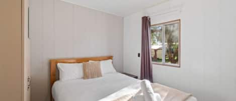 Een slaapkamer met een bed, een raam met gordijnen en een deur.