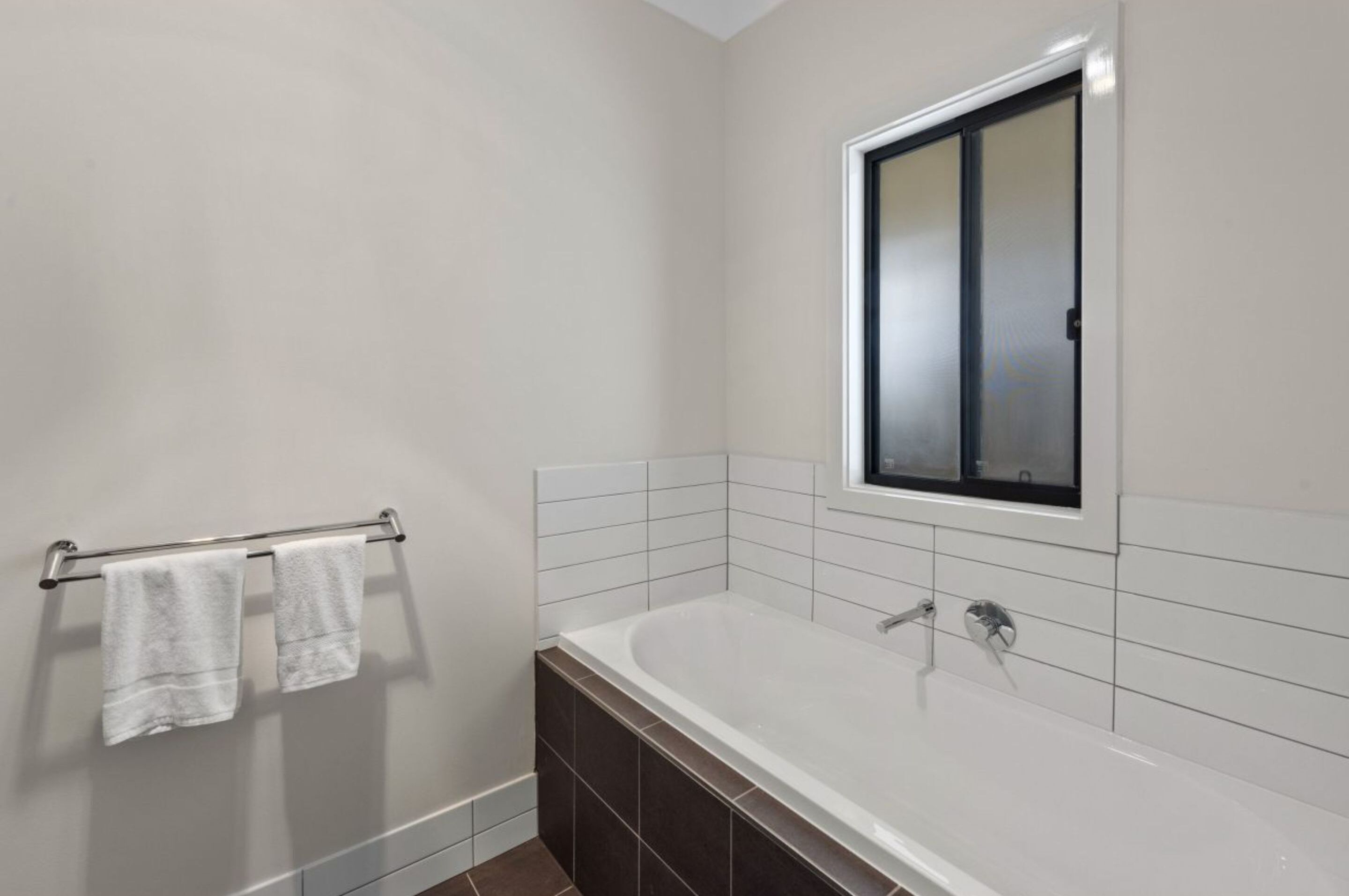 A modern bathroom with a white bathtub, a towel rack with two towels, and a large mirror above the tub.