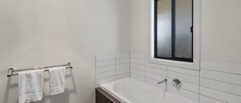 A modern bathroom with a white bathtub, a towel rack with two towels, and a large mirror above the tub.