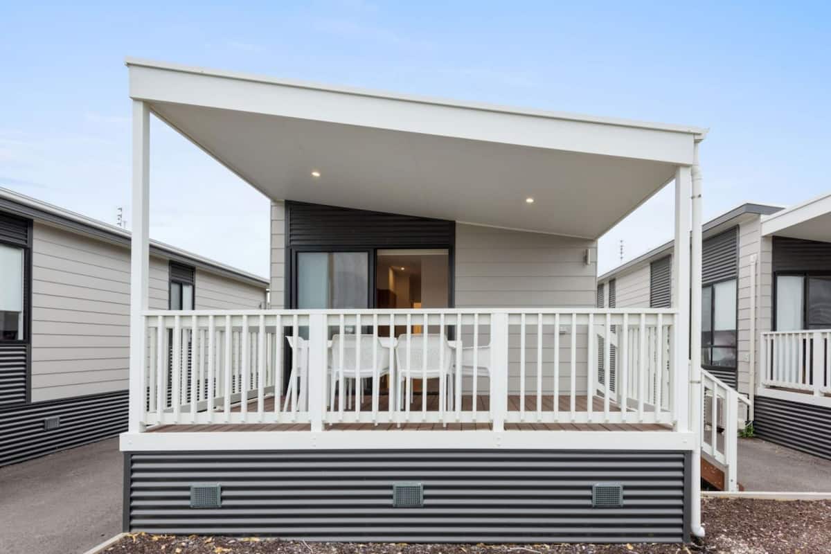 A modern building with a covered outdoor area, white railings, and a table with chairs.