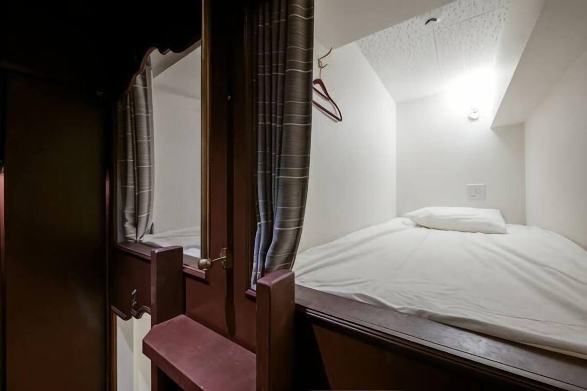 A bedroom with a bed, a nightstand, a mirror, and a hanging coat rack.