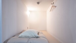 Una habitación estrecha y bien iluminada con una cama al fondo, una lámpara en el techo y un gancho en la pared.