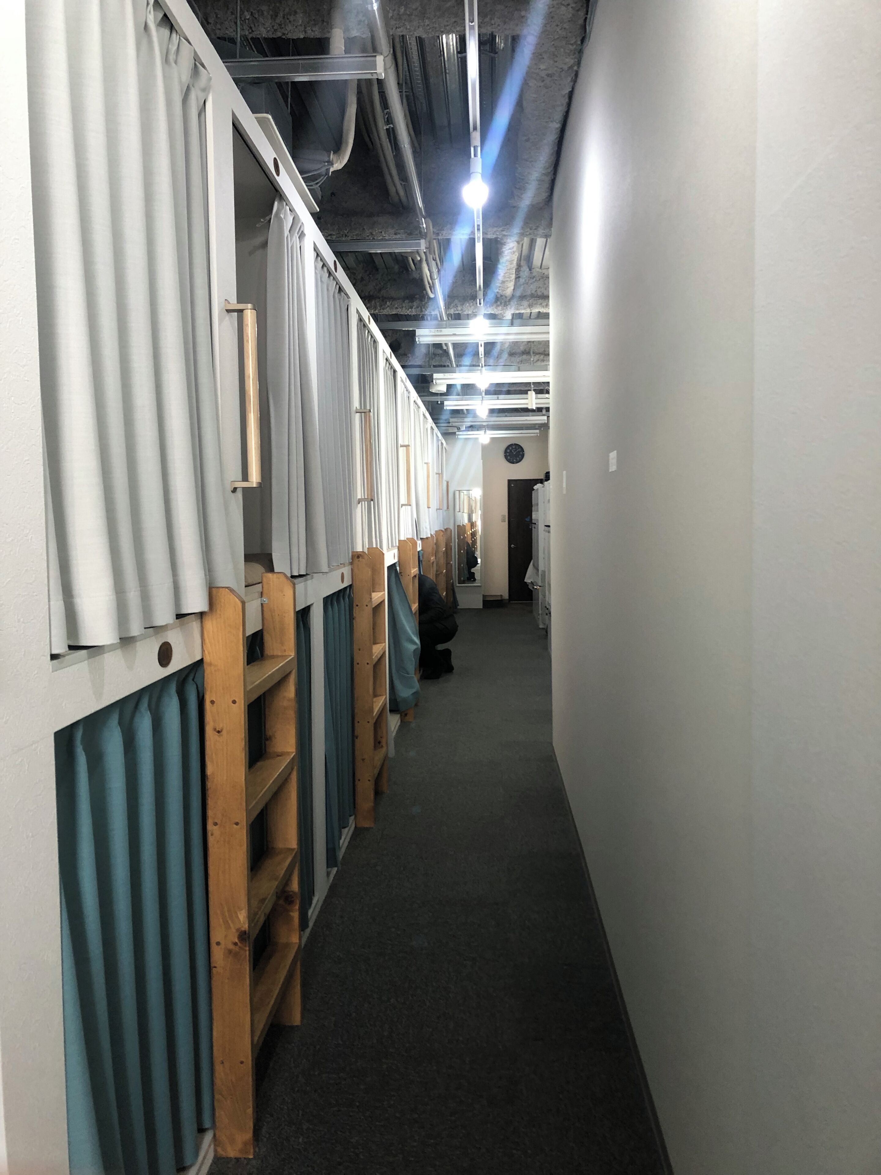 Un pasillo con literas, estanterías de madera y cortinas.