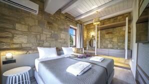 Une chambre avec un mur en pierre, un lit avec une literie blanche, une table de chevet et une lampe.