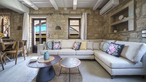 Un salon avec un mur en pierre, un canapé beige, une table à manger avec des chaises et une table basse.
