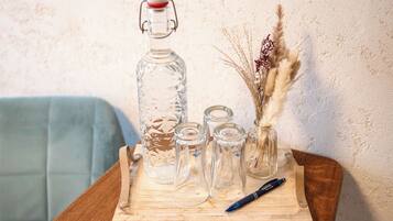 A wooden tray with a glass decanter, small glass bottles, a pen, and dried plants on a table.