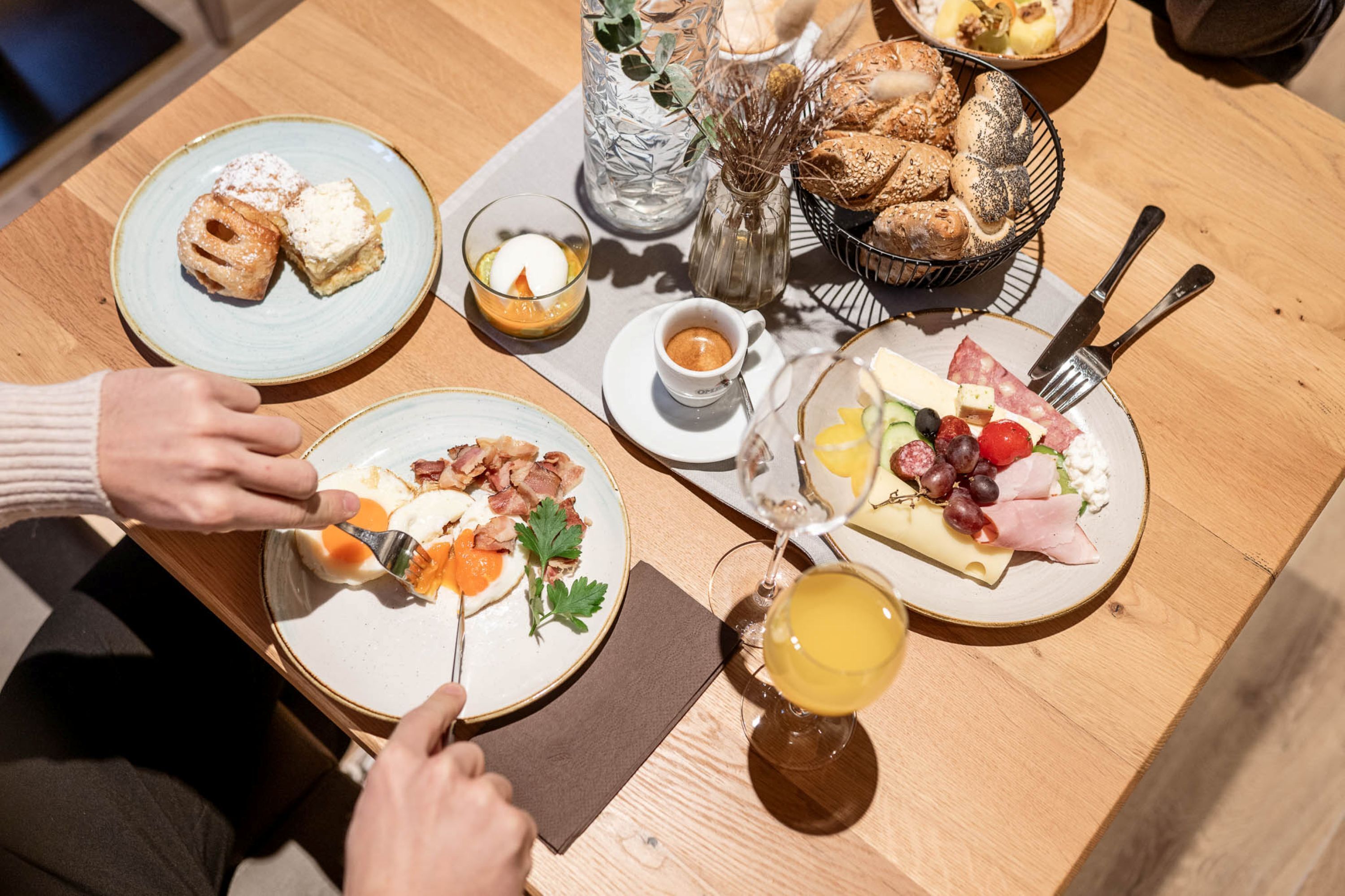 A breakfast setting with plates of food, a glass of juice, and a basket of pastries.