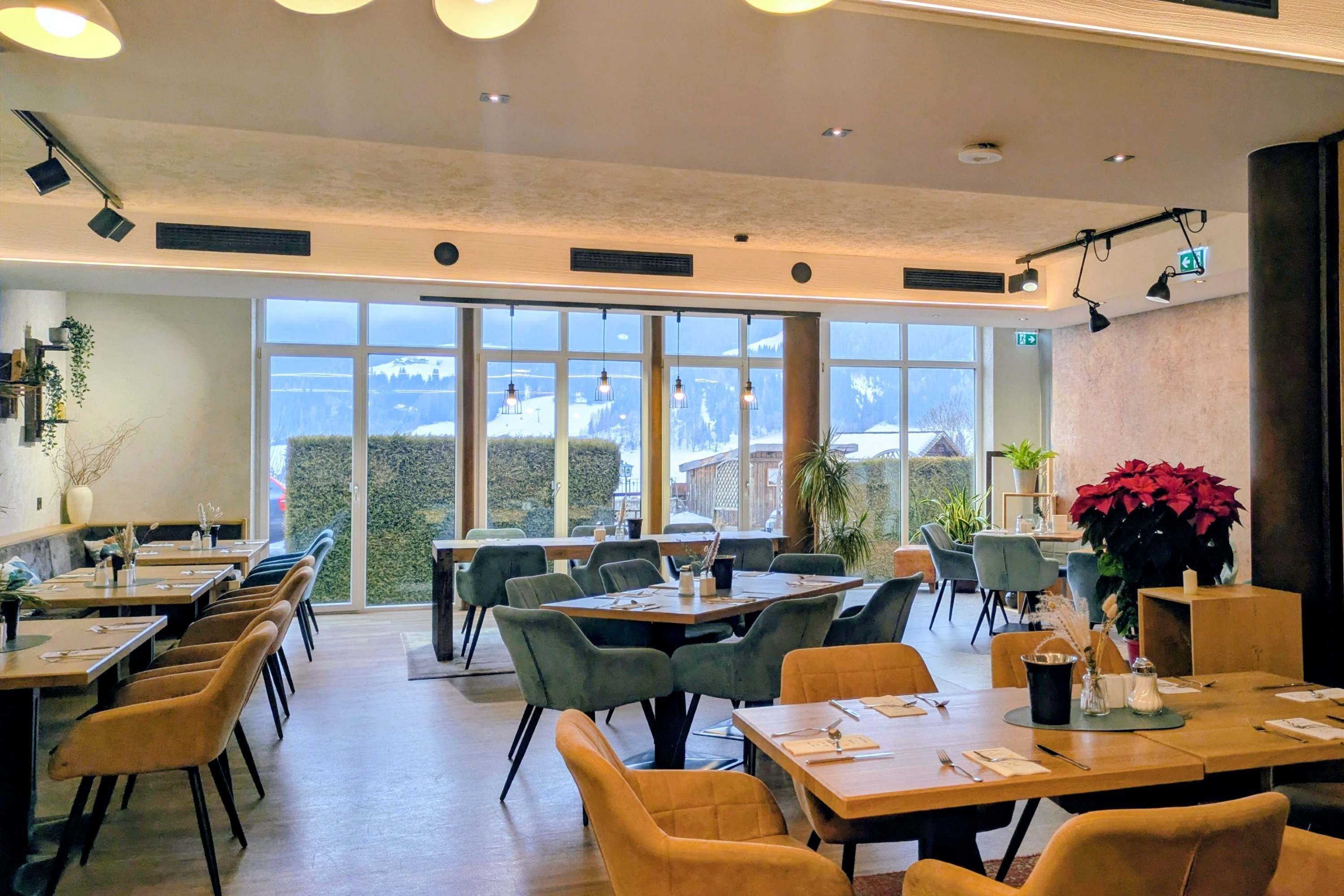 A modern dining area with tables and chairs, large windows, and indoor plants.