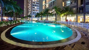 A nighttime swimming pool surrounded by high-rise buildings with balconies, palm trees, and a white picket fence. - Park Hill Times City Apartment						 						 (Hanoi)