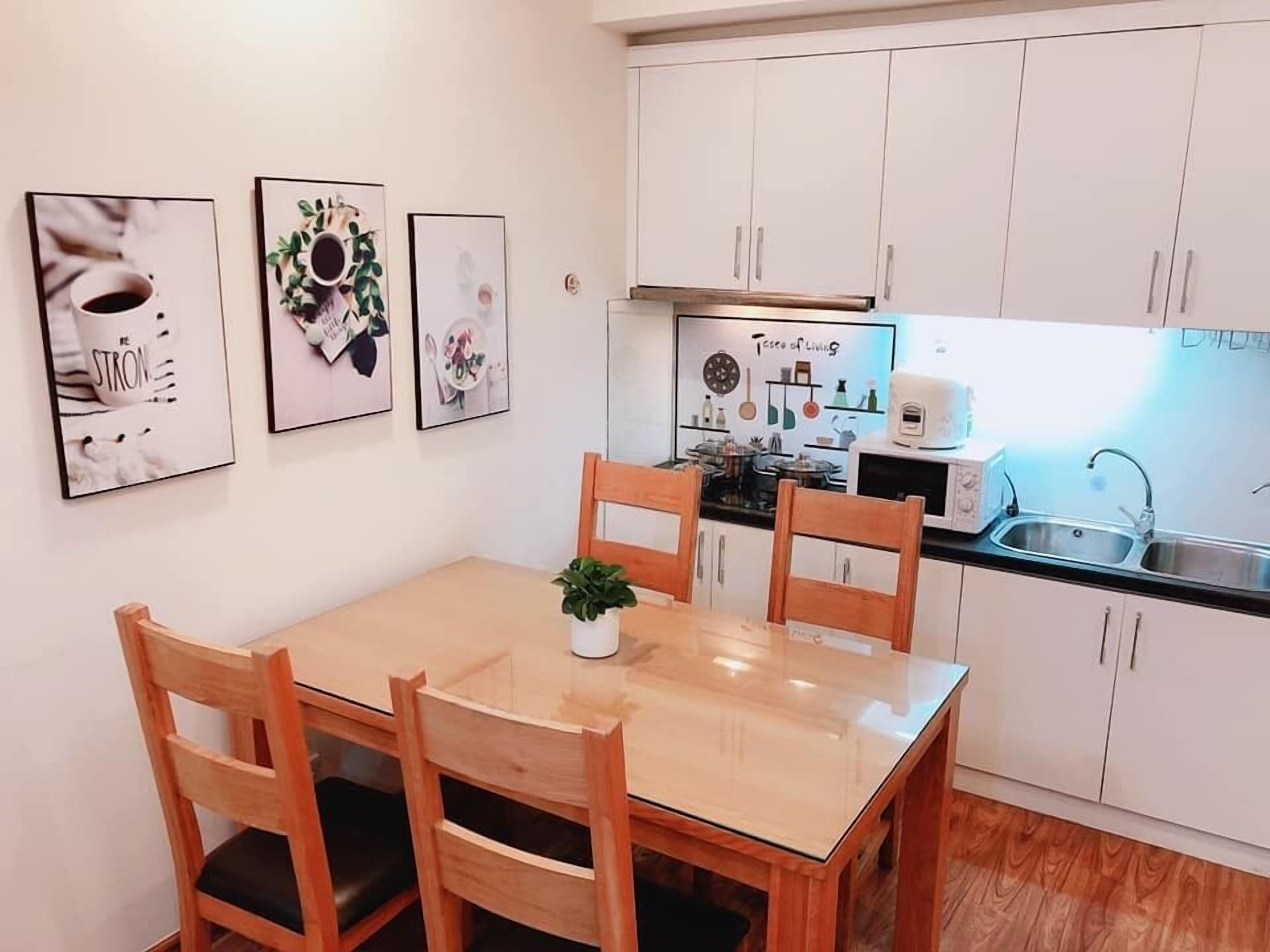 Una cocina compacta con armarios blancos, una mesa de madera con cuatro sillas y una pequeña planta en maceta.