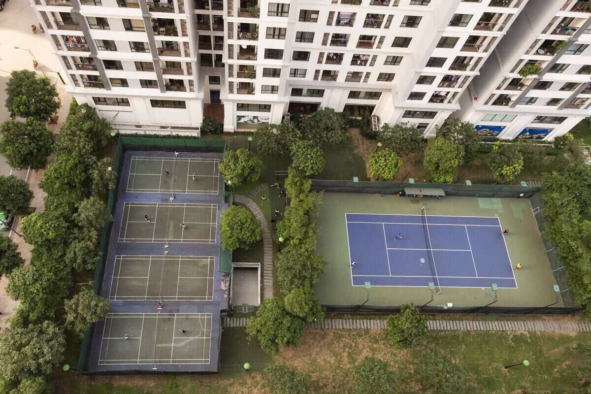 Un edificio de gran altura con múltiples balcones y un complejo de canchas de tenis.