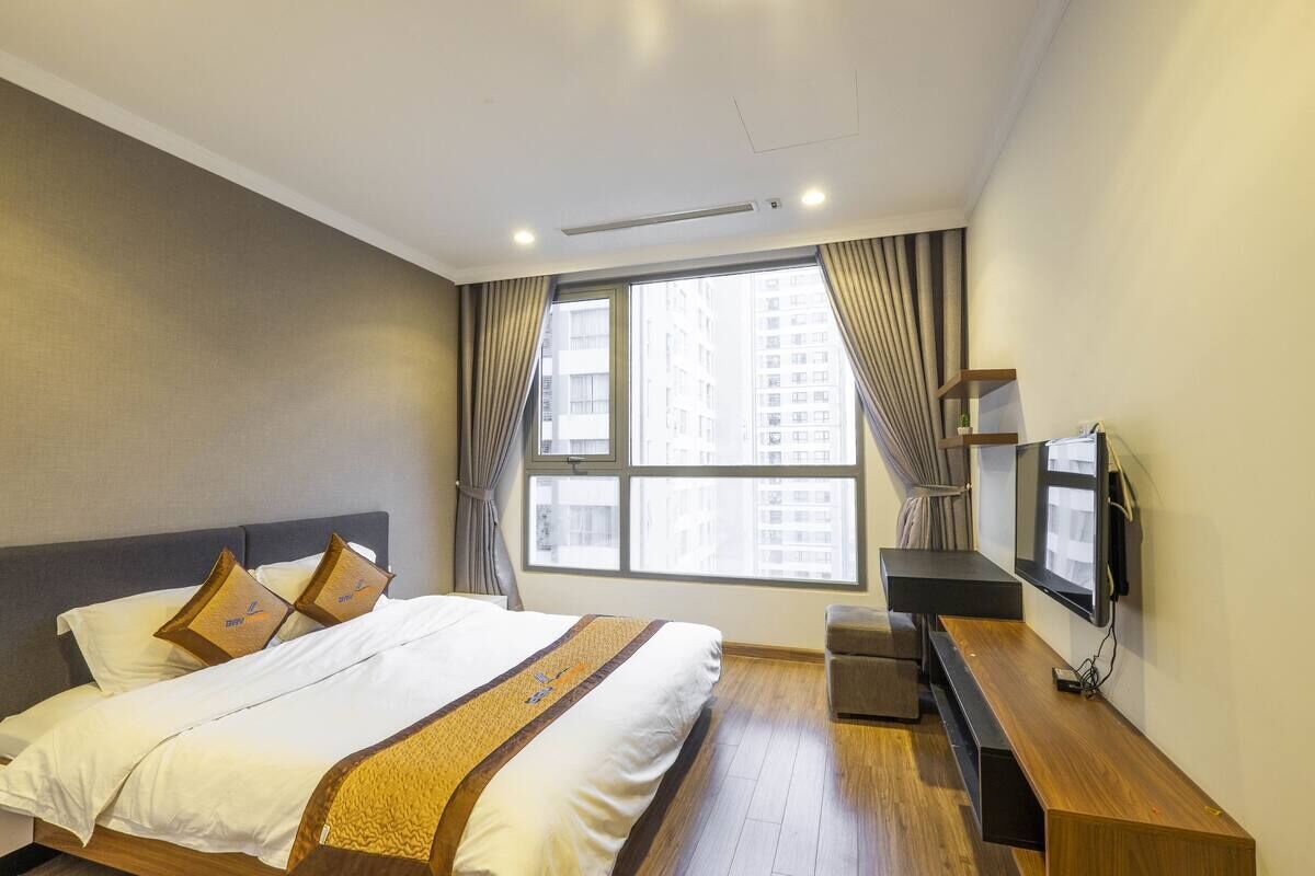 A modern hotel room with a large bed, a TV mounted on the wall, and a window with curtains.