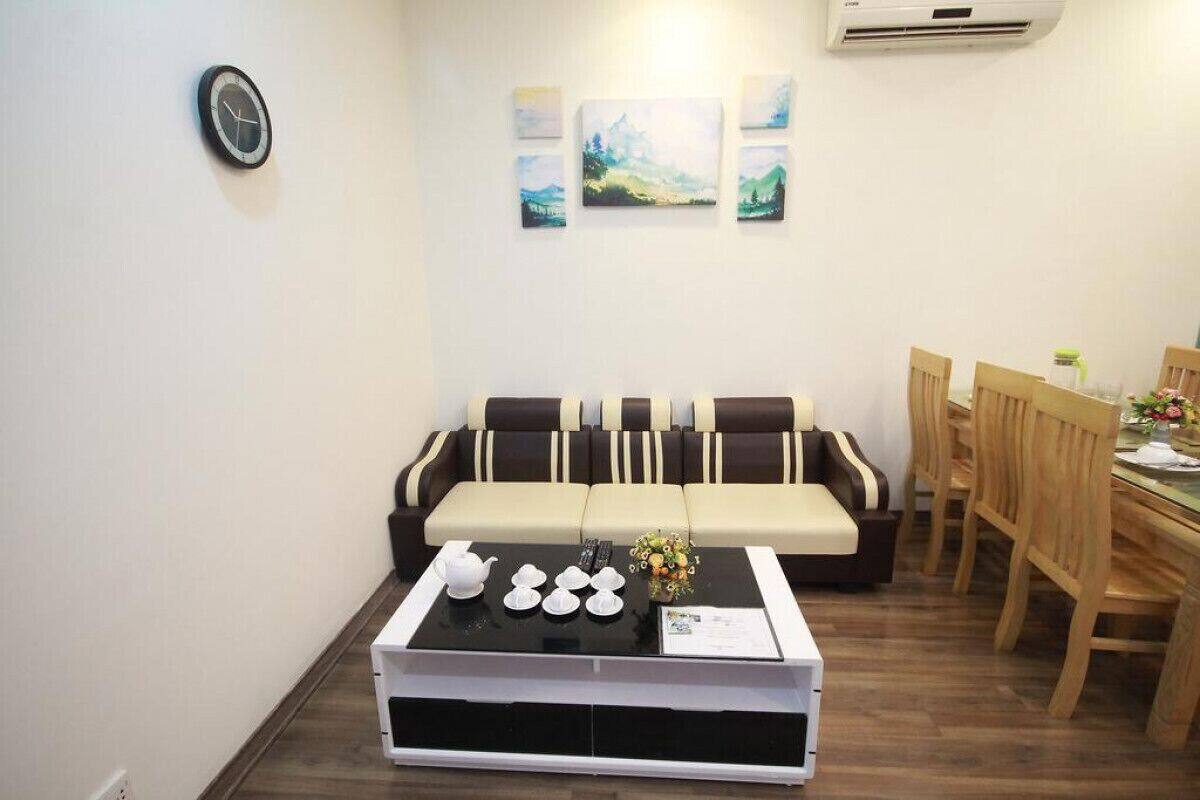 A living room with a sofa, a coffee table with teacups, a clock, and paintings on the wall.
