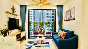A modern living room with a sofa, TV, and a view of tall buildings through large windows. - Park Hill Times City Apartment						 						 (Hanoi)