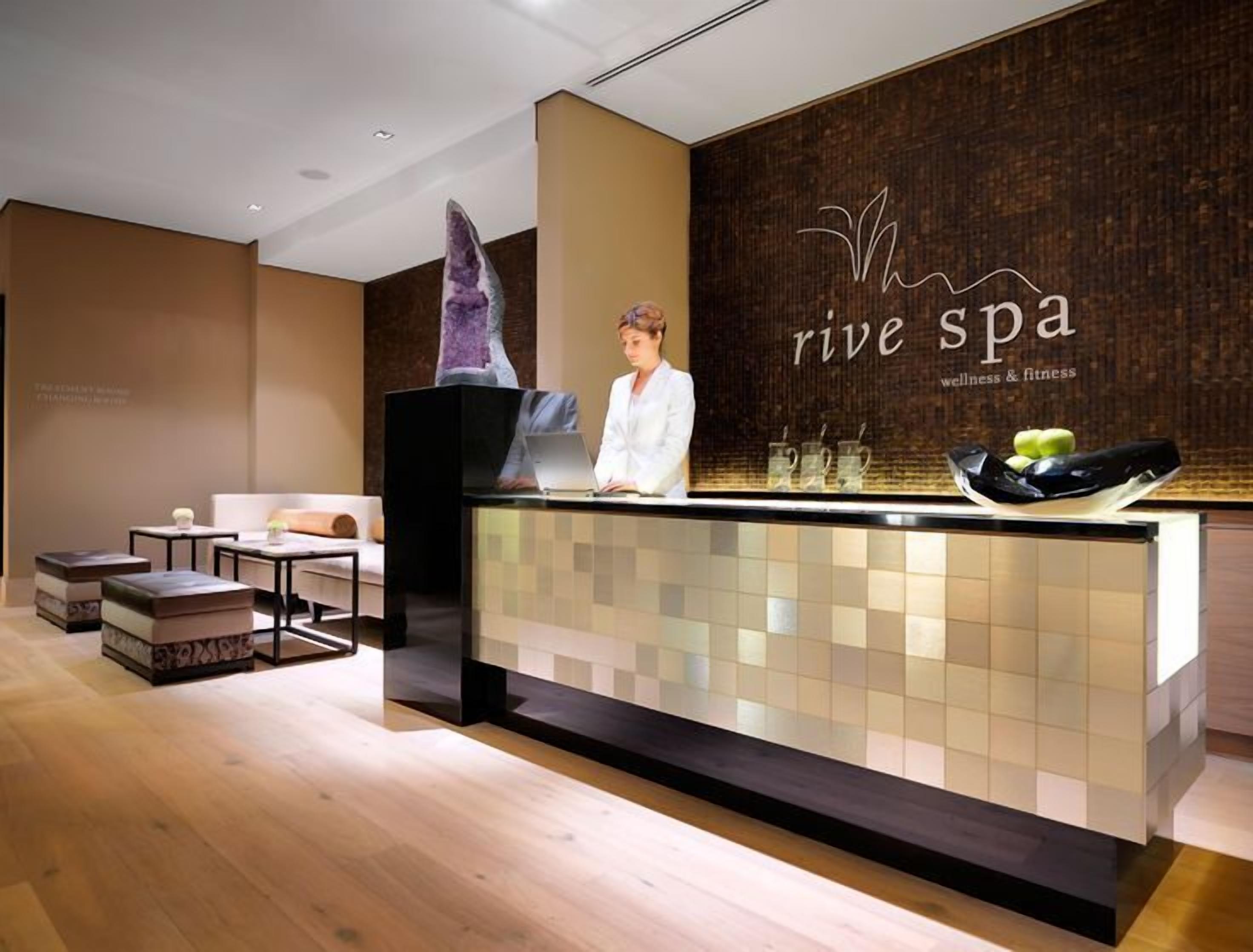 Un espace d’accueil avec une réceptionniste, un comptoir d’accueil et un mur portant le nom du spa.