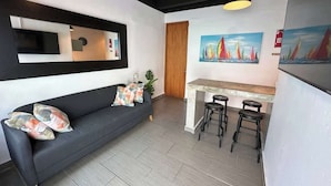 Ein stilvoller Wohnbereich mit Sofa, Fernseher, einem Gemälde und einer Bar mit Hockern.