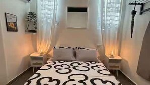 Ein Schlafzimmer mit einem Bett, zwei Nachttischen, einem Fenster mit Vorhängen und einer Wand-Klimaanlage.