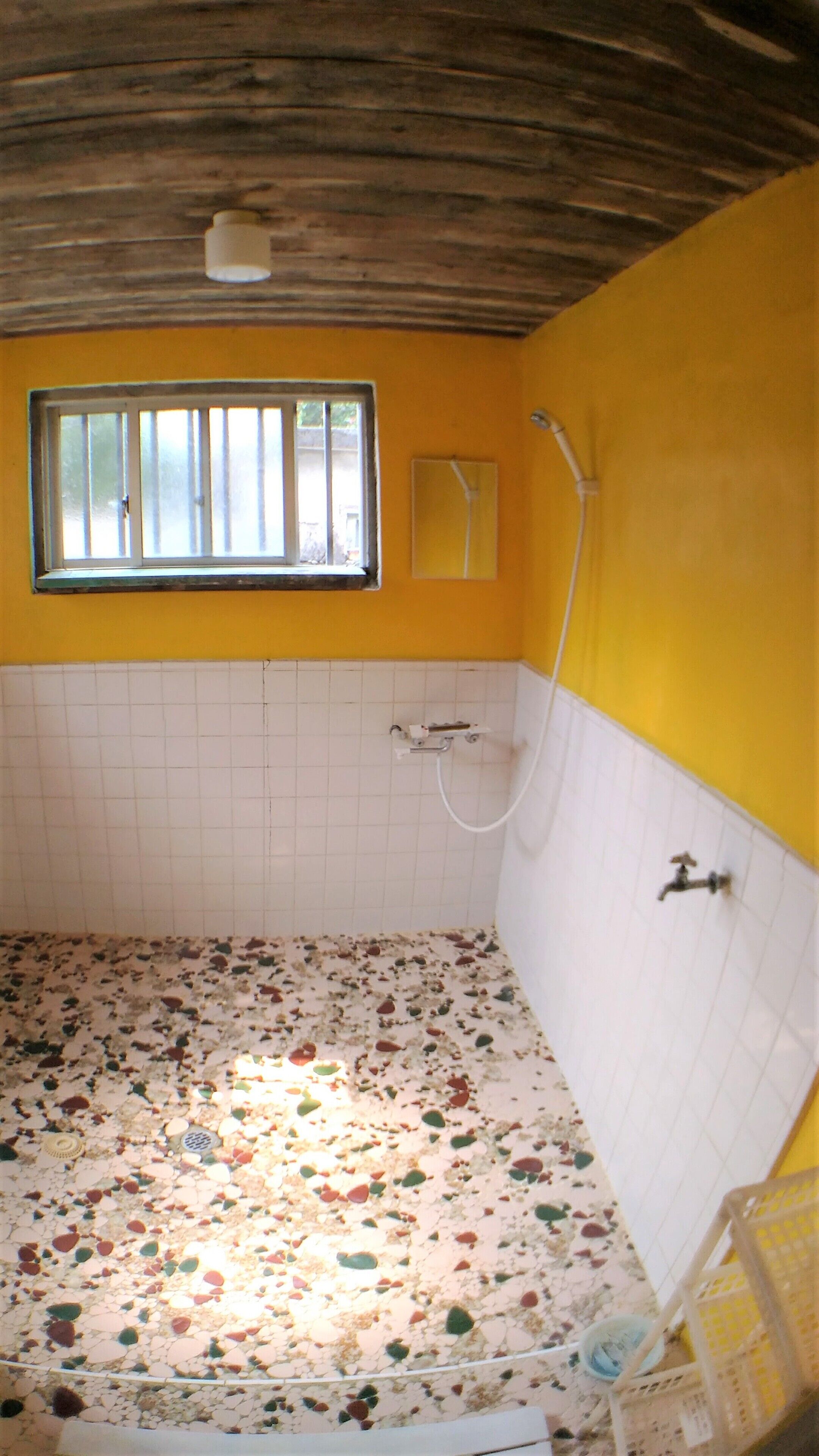 A bathroom with a tiled floor, a shower, a window, and a yellow wall.