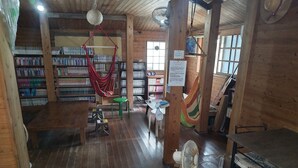 Een houten interieur met boekenkasten, een hangmat, een ventilator en een tafel.