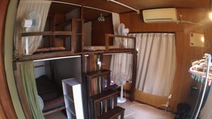 Een kleine kamer met een stapelbed, een bureau, een stoel, een ventilator en een airconditioning.
