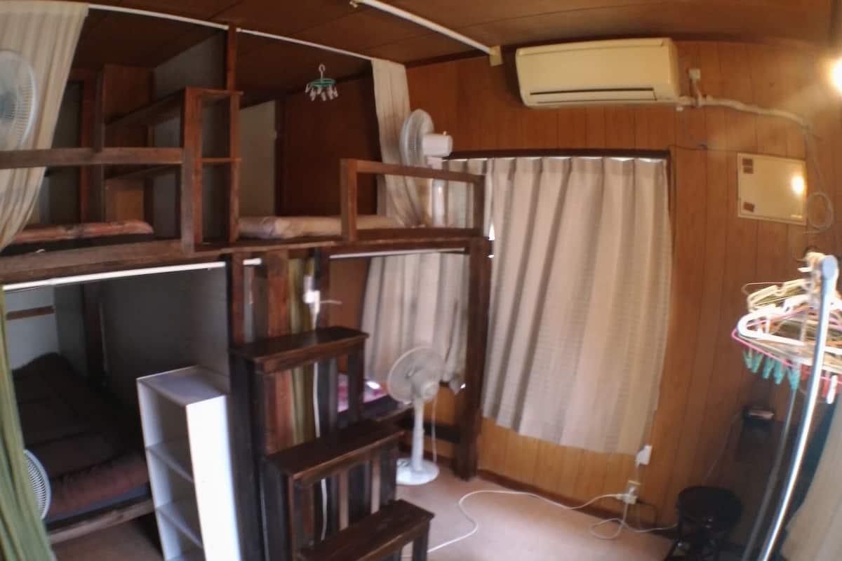 Habitación pequeña con literas, un escritorio, una silla, un ventilador y aire acondicionado.