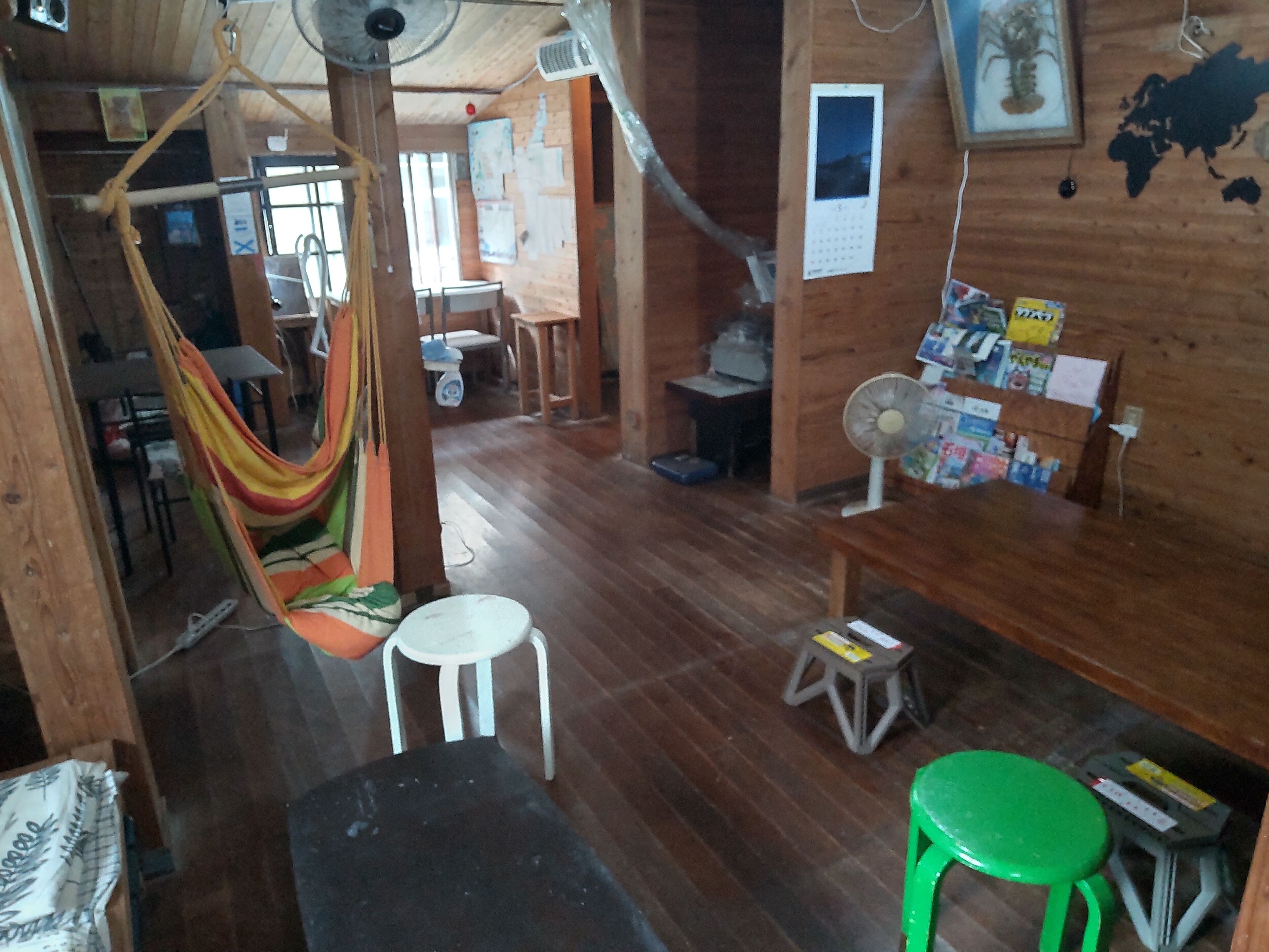 Una habitación de madera con una hamaca, un ventilador, un taburete verde y una mesa con revistas.