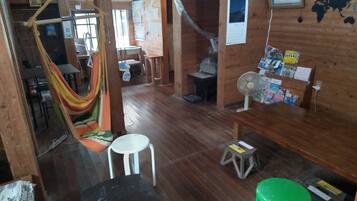 Una habitación de madera con una hamaca, un ventilador, un taburete verde y una mesa con revistas.
