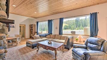Un salon chaleureux avec un plafond en bois, un ensemble de canapés, un fauteuil en cuir, une table basse et une bibliothèque.