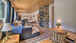 A cozy living room with a stone fireplace, wooden ceiling, and a comfortable seating area with a couch and a coffee table. - Secluded Camp Connell Home w/ Deck + Fireplace! (Camp Connell)