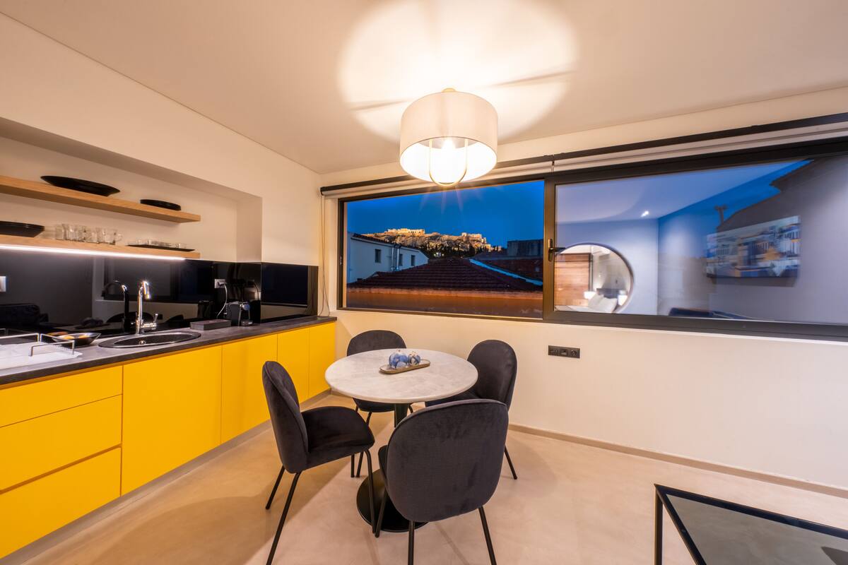 Une cuisine moderne avec des meubles de couleur jaune, une table de salle à manger ronde entourée de chaises et une grande fenêtre donnant sur la ville.