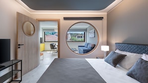 Une chambre d’hôtel moderne avec un grand lit, un miroir rond, une télévision et une vue sur l’extérieur.