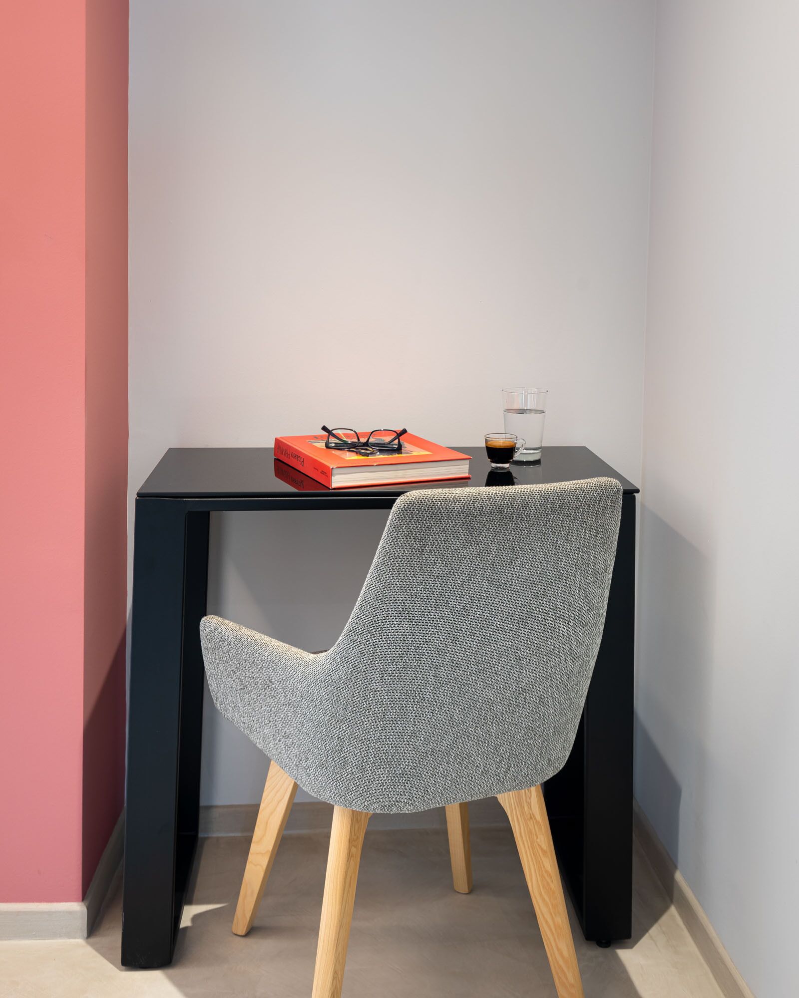 A small, modern desk with a chair, a book, glasses, and a glass of water.
