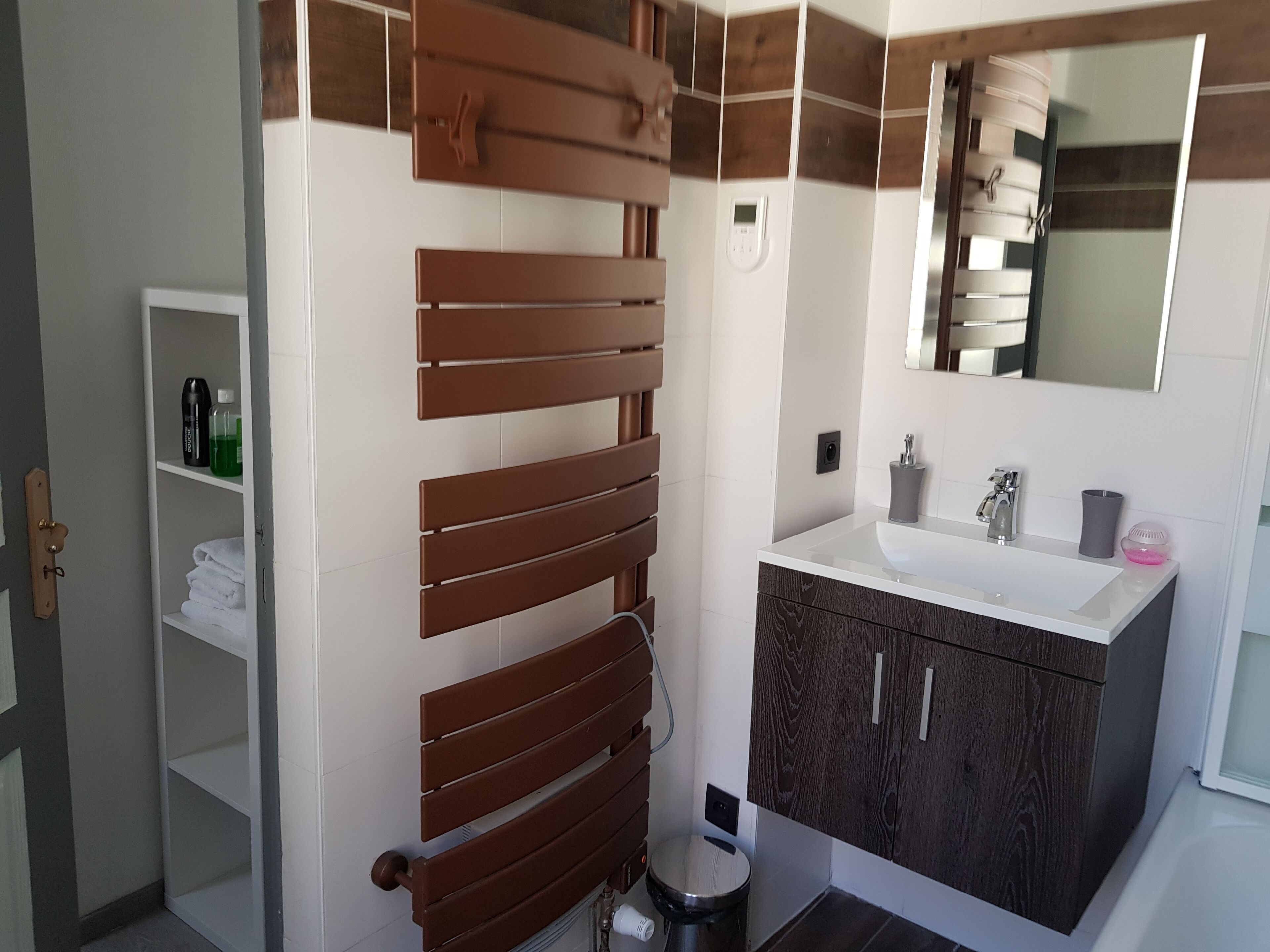 Une salle de bain moderne avec un radiateur en bois, un lavabo blanc surmonté d’un miroir et un meuble en bois foncé.