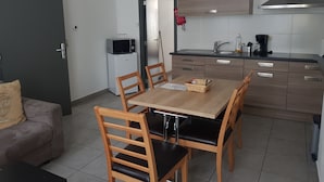 Een kleine keuken met een eettafel, stoelen, een magnetron en een koelkast.