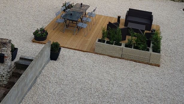 Een terras met een tafel en stoelen, omgeven door plantenbakken en een stenen muur.