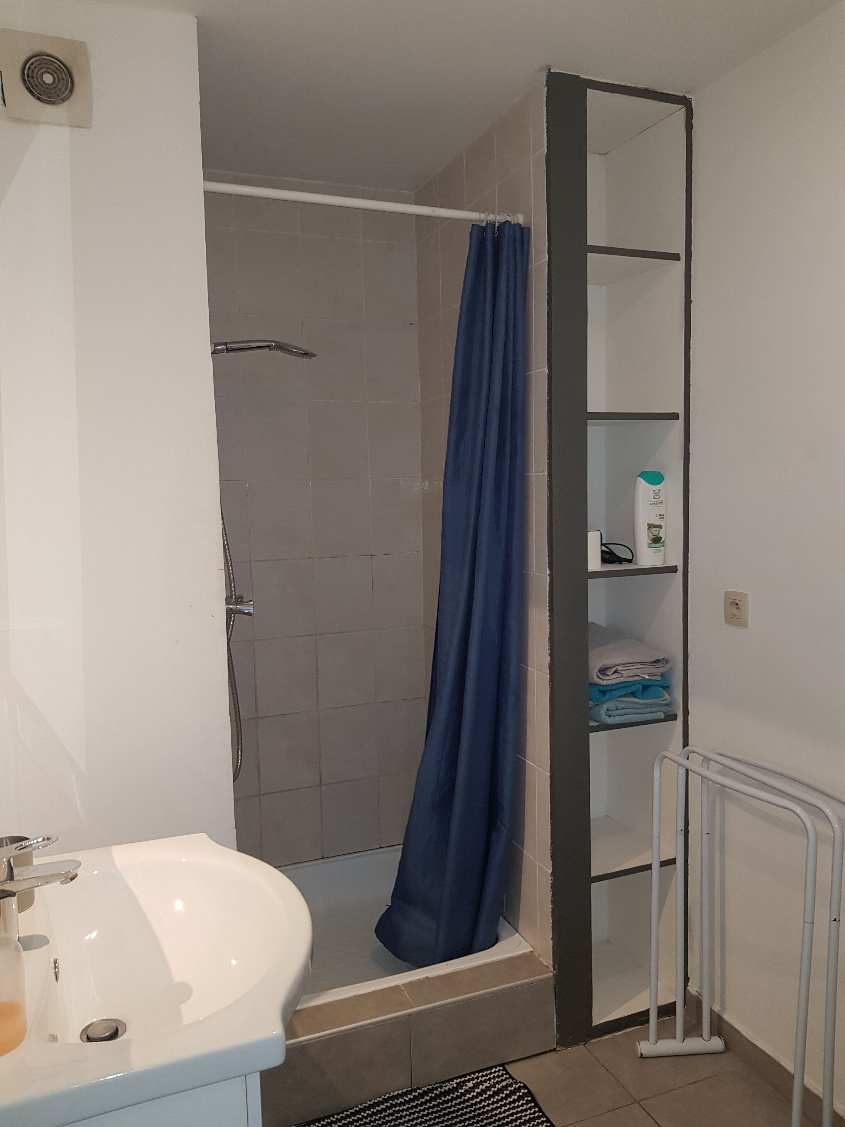 Een badkamer met een douche, wastafel en een plank met opgevouwen handdoeken.