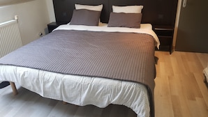 Een slaapkamer met een groot bed, een donker hoofdbord en een houten vloer.