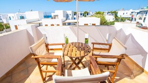 A terrace with wooden furniture, a yellow umbrella, and a view of white buildings. - Summer Dream II (Naxos)