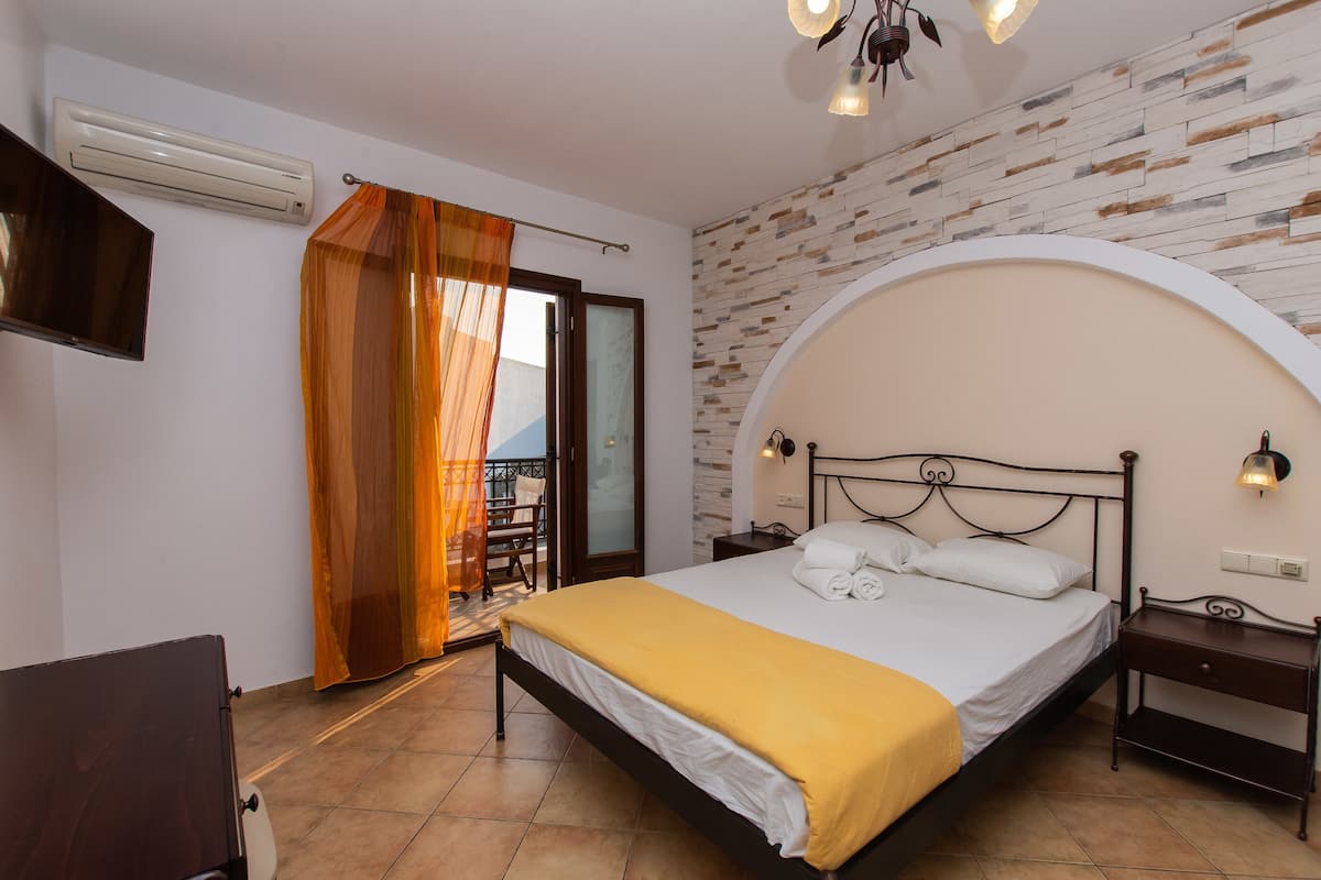 A bedroom with a bed, a nightstand, a TV, and a balcony with a view.