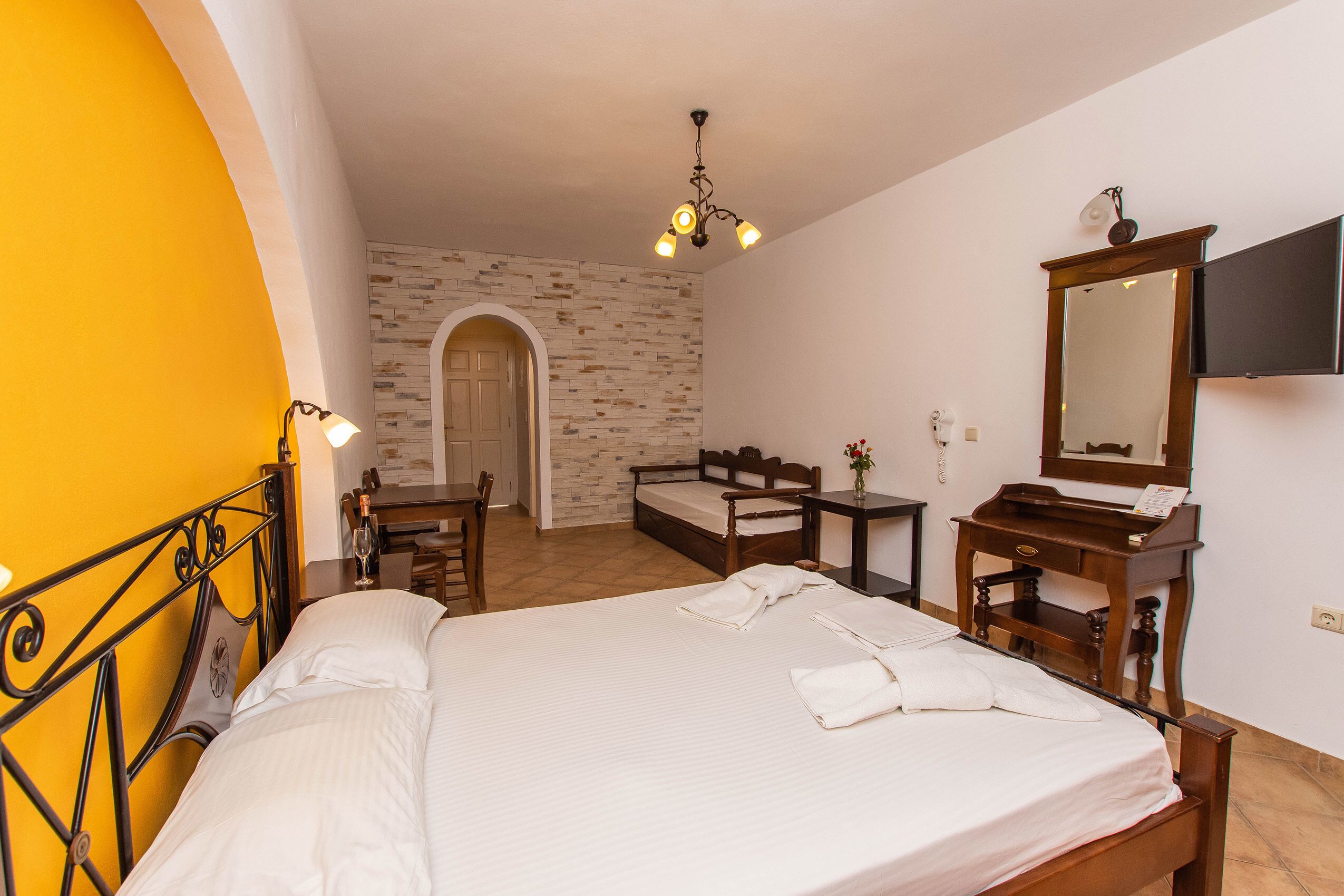 A hotel room with a bed, a desk, a chair, a mirror, and a small table.