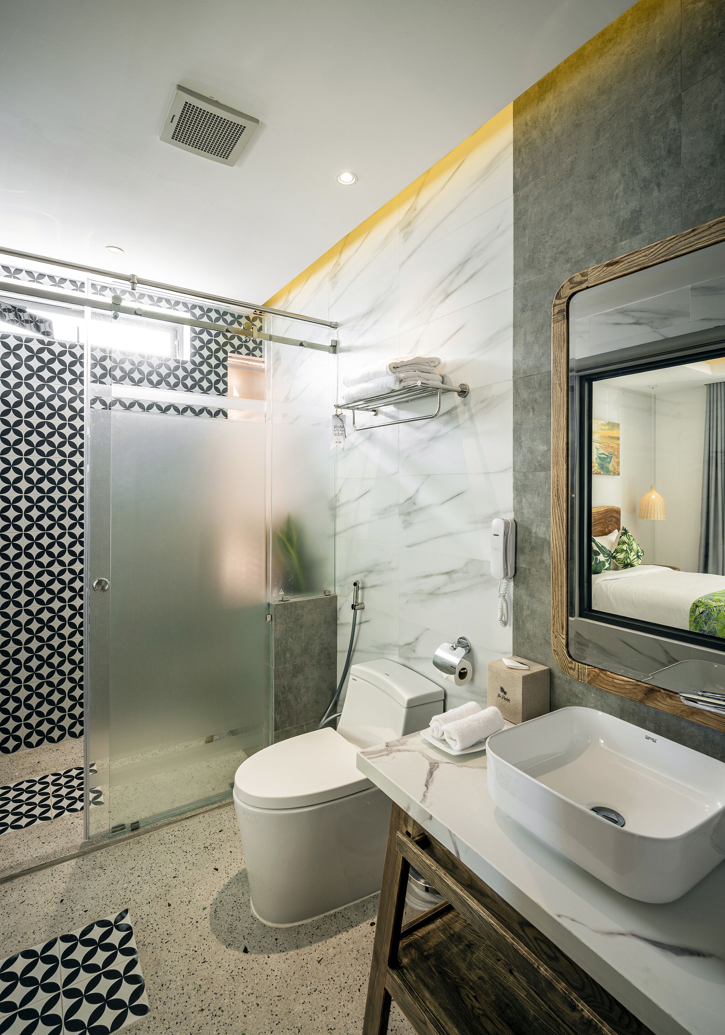 A modern bathroom with a glass-enclosed shower, a white toilet, a large sink, and a mirror with a wooden frame.