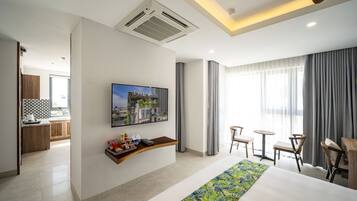 A hotel room with a large bed, a TV mounted on the wall, a small kitchen area, and a balcony with curtains.