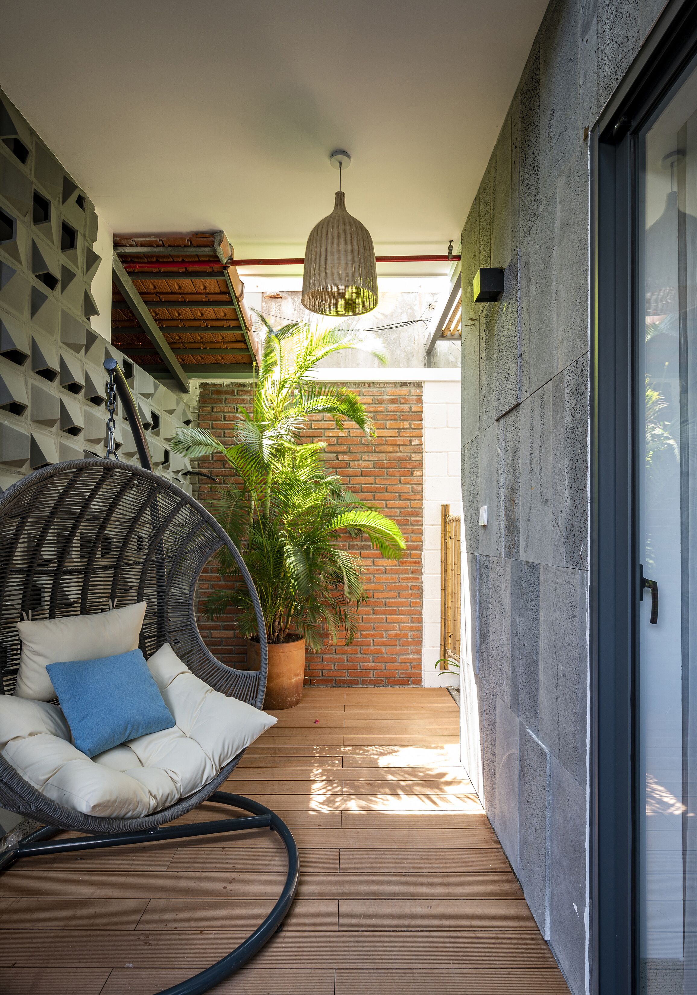 Un balcon avec un fauteuil en osier, un pot de fleurs et une suspension lumineuse.