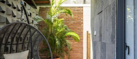 A balcony with a wicker chair, a potted plant, and a hanging light fixture.